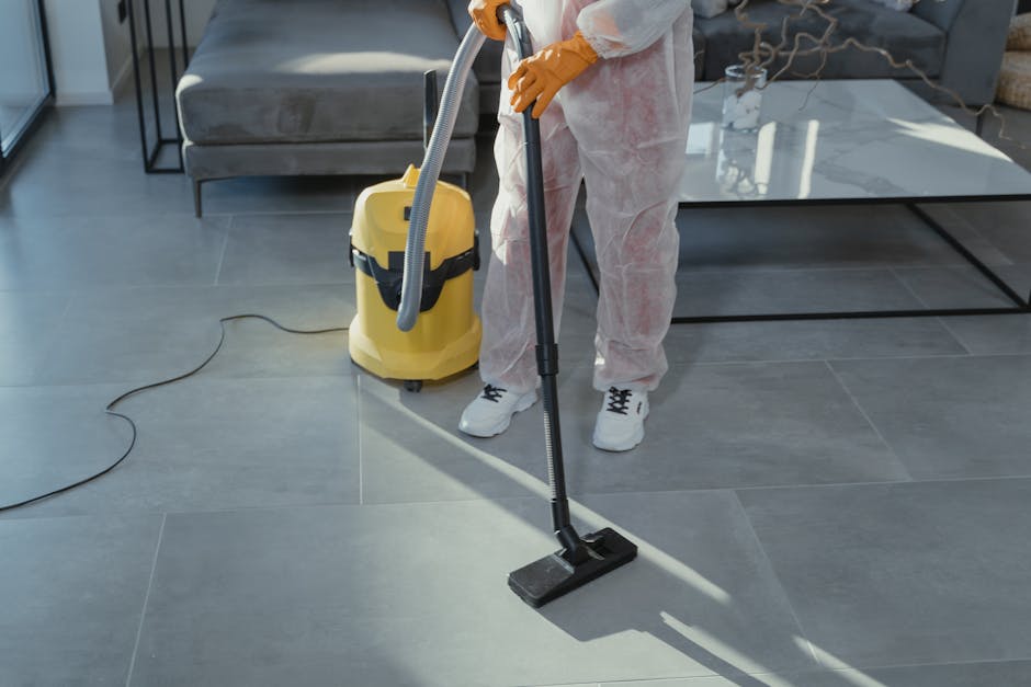 A female cleaner with short dark hair using a cloth to wipe the glass door of a refrigerator in a modern kitchen. The surface of the refrigerator appears clean and reflective with a shiny stainless st